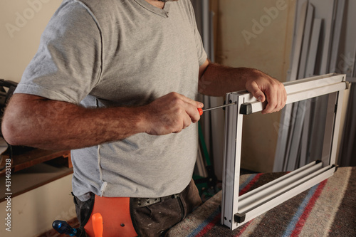 Man screwing an aluminum window. Working in a carpentry shop. Construction of openings for houses. Horizontal image.