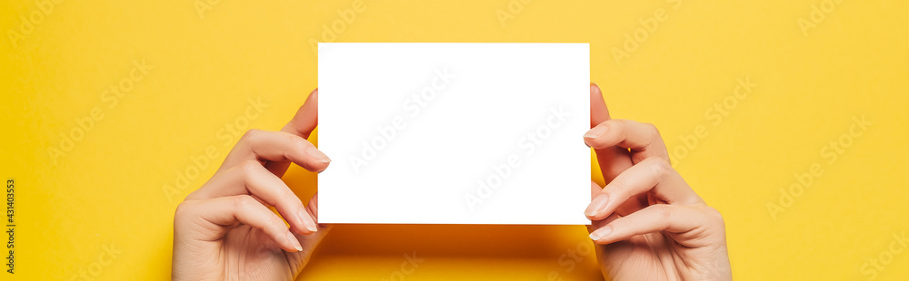 Female hands hold a blank sheet of paper on a yellow background. Advertising space