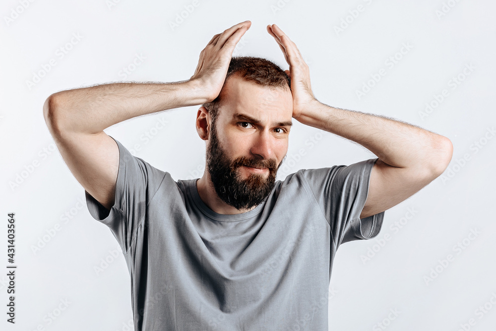 Portrait of handsome young man frowning while holding hands near head on white background with space for advertising mock up Portrait of handsome young man frowning while holding hands near head on white background with space for advertising mock up