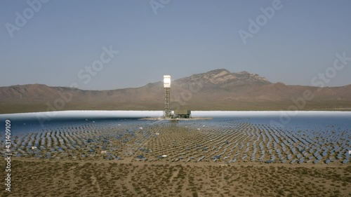 Aerial Panning Across A Solar Field In The Desert With Dirt, Dry Brush, Clear Blue Sky, Bright Sunlight, And Steep Mountains In The Background - Ivanpah, California photo