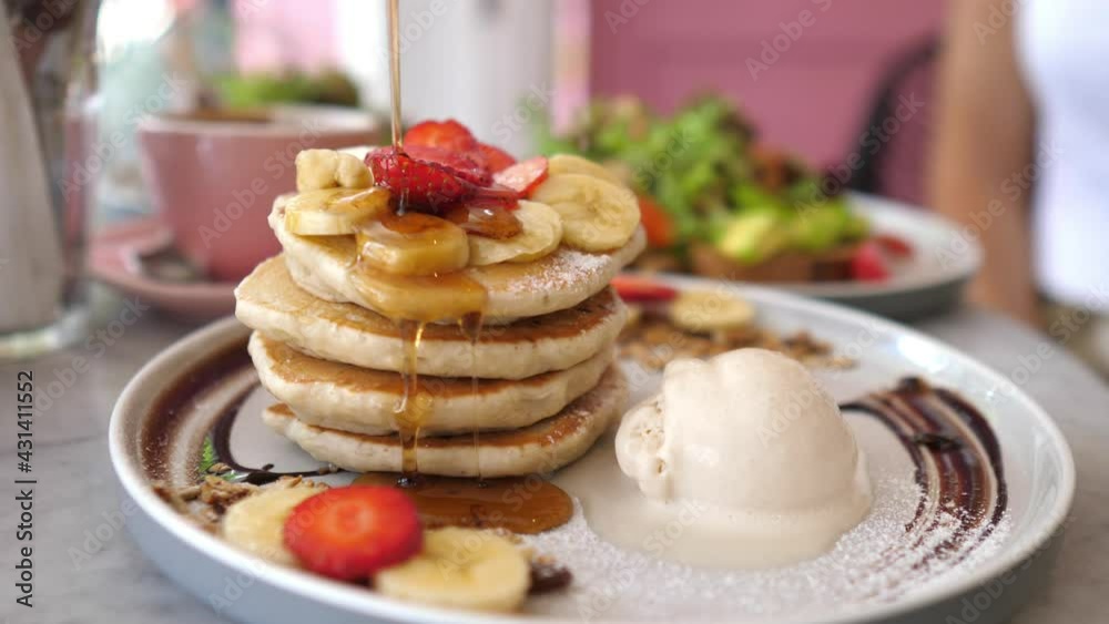 Sweet american breakfast. Pouring syrup over stack of fluffy pancakes served with scoop of ice cream and berries Sweet american breakfast. Pouring syrup over stack of fluffy pancakes served with scoop of ice cream and berries