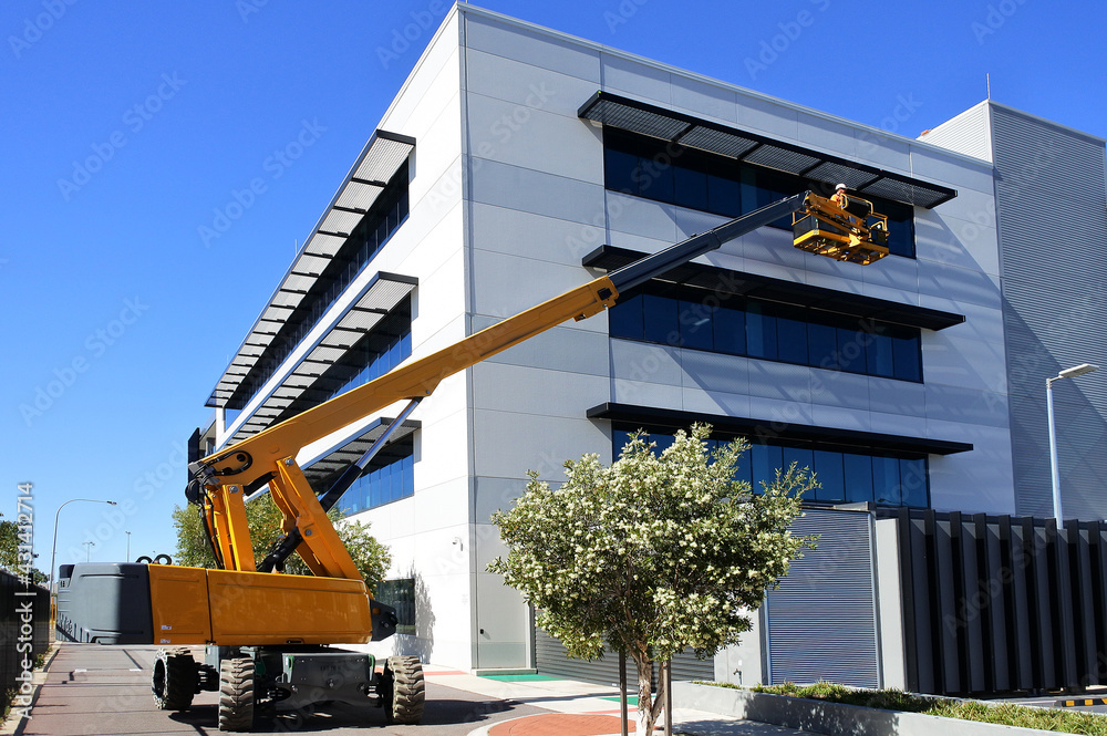 Worker using an articulated boom lift beside a building exterior