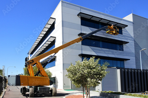 Obraz na płótnie Worker using an articulated boom lift beside a building exterior w salonie