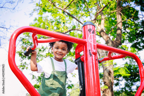 Cute African American little kid boy funny while playing on the Exercise machine in the daytime in the spring season. Outdoor activity. Playing make-believe the concept. Outside education