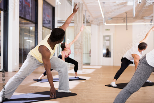 Portrait of focused African American man performing set of pilates exercises with group in fitness studio