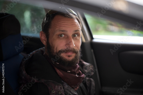 Fashion Portrait of Bearded man sitting in a car cabin and looking at camera, selective focus. Attractive elegant happy Man sitting in new car. Travel is good for the soul. Cheerful hipster guy