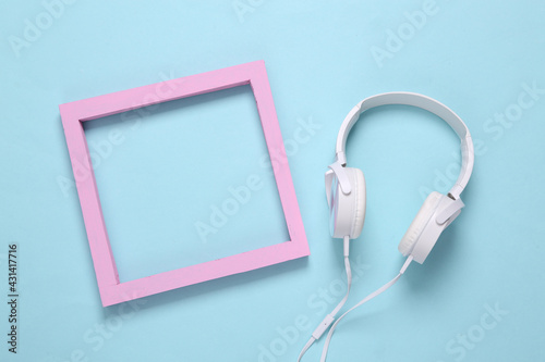 White stereo headphones and pink blank frame on a light blue background. Copy space