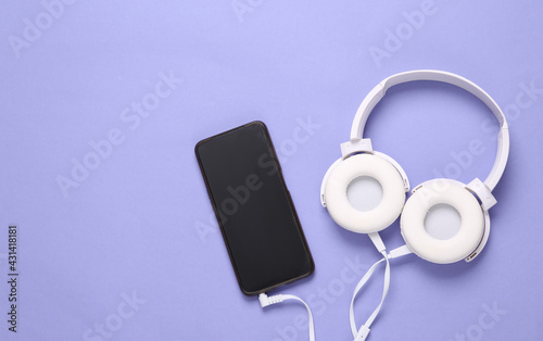 Stereo headphones with smartphone on purple background. Top view
