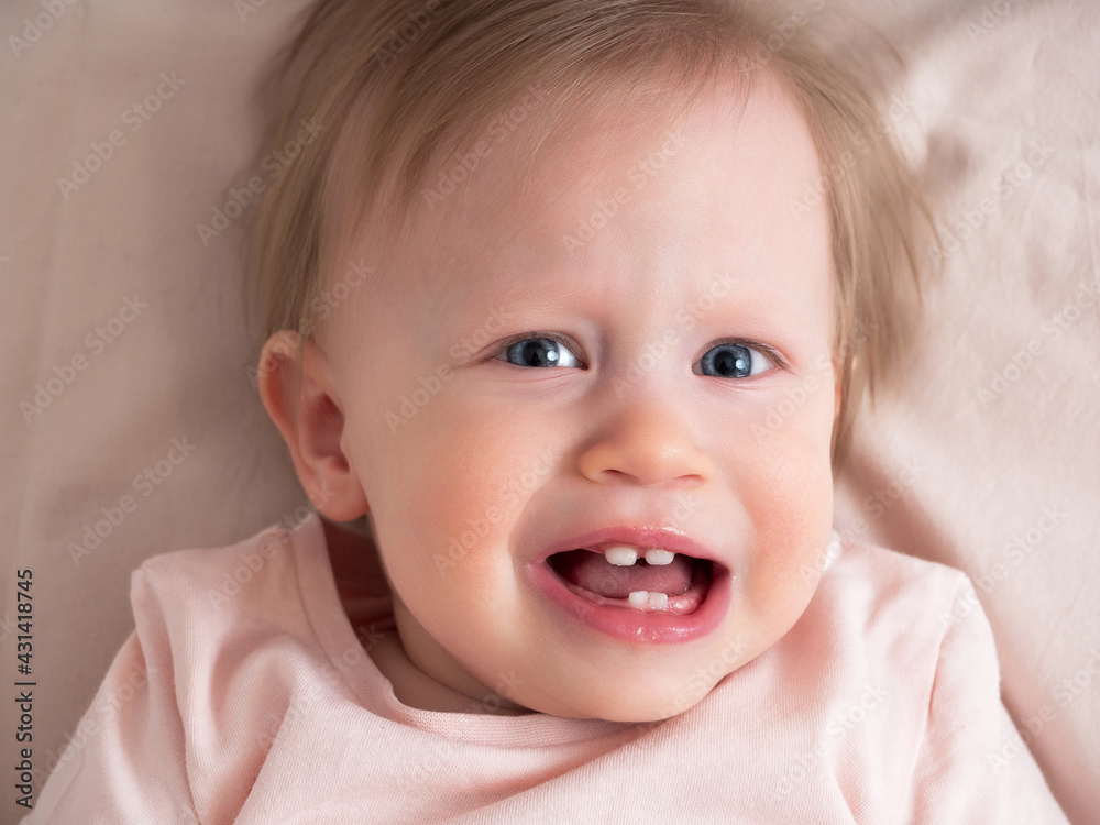 A little baby girl is suffering from pain, teething, looking at the camera, crying, close-up. Portrait of a beautiful light girl in pink tones. Child age one year A little baby girl is suffering from pain, teething, looking at the camera, crying, close-up. Portrait of a beautiful light girl in pink tones. Child age one year