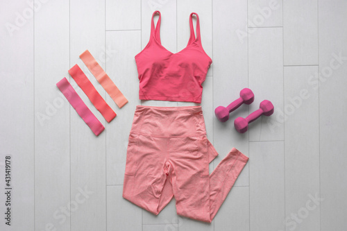 Fitness clothes flat lay workout at home with resistance bands and dumbbell weights. Pink athleisure fashion clothing top view on white wood floor. photo