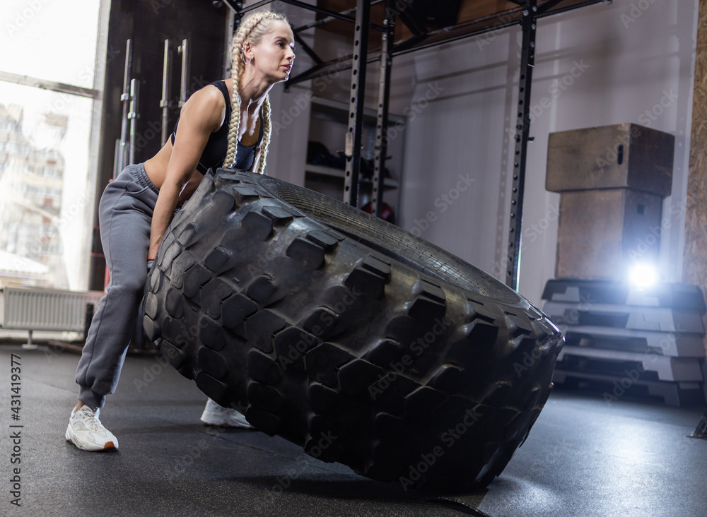 Fit female athlete flipping huge tire. Woman lifts a heavy wheel. Muscular young woman doing