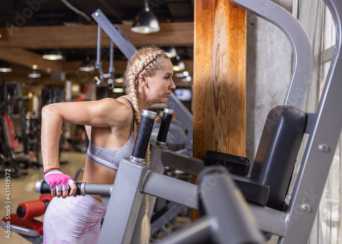 Young fit blonde woman with long pigtails does push-ups on the uneven bars in the modern gym. Fitness workout, healthy lifestyle concept