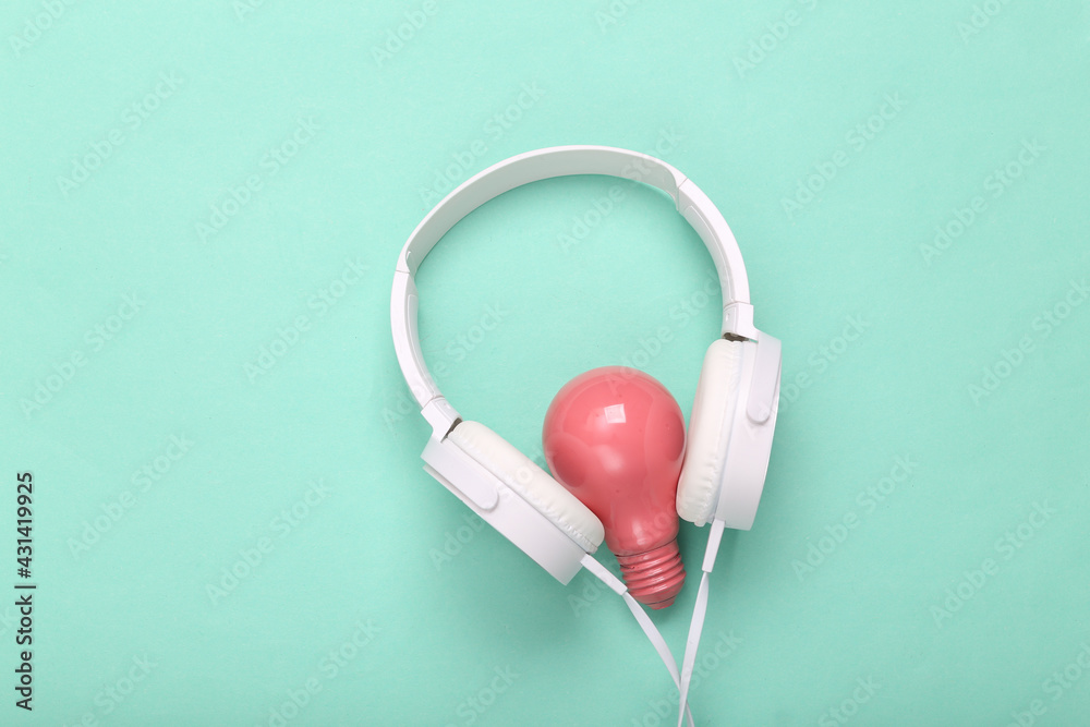 Stereo headphones with pink light bulb on blue background. Minimalism music concept. Creative layout. Fresh idea.