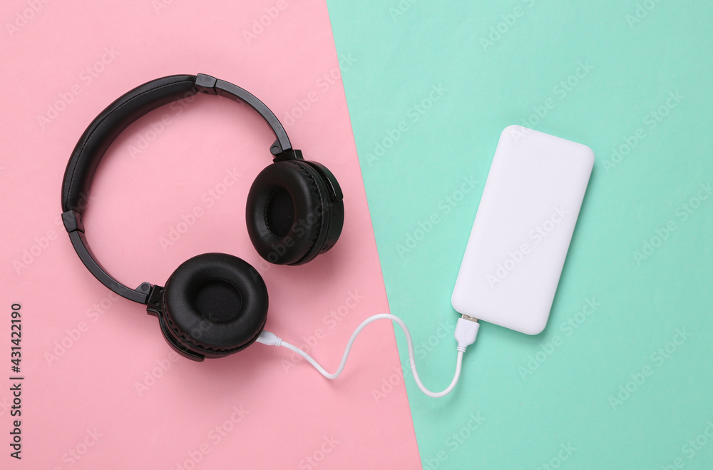 Wireless headphones and External portable battery (power bank) on pink blue background. Top view. Flat lay Wireless headphones and External portable battery (power bank) on pink blue background. Top view. Flat lay