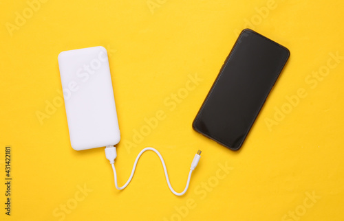 Smartphone and External portable battery (power bank) on yellow background. Top view. Flat lay photo