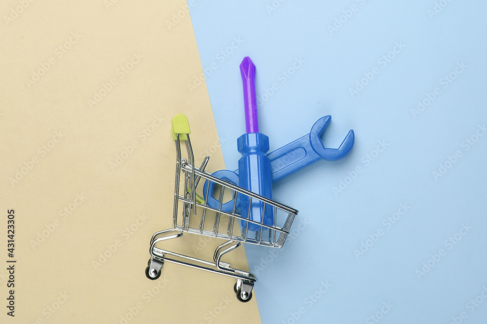 Mini shopping trolley with toy work tool on a blue-yellow pastel background. Repair concept. Top view Mini shopping trolley with toy work tool on a blue-yellow pastel background. Repair concept. Top view