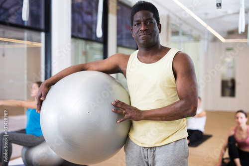 Portrait of man pilates trainer standing with fitness ball during group training at yoga studio