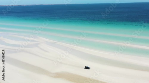 2020 - Excellent aerial shot of a van driving along the shoreline white sands of Flaherty Beach near clear blue waters. photo