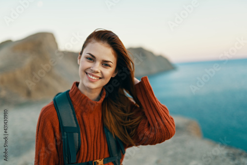 happy woman in a sweater with a backpack on her back smiling on nature in the mountains near the sea