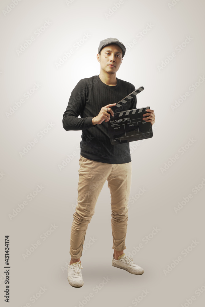 Photo of Asian guy, holds clapperboard, being producer of new film, smiles broadly, wears casual t shirt. Cheerful man inbolved in movie making, isolated on white wall Photo of Asian guy, holds clapperboard, being producer of new film, smiles broadly, wears casual t shirt. Cheerful man inbolved in movie making, isolated on white wall