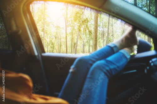 Closeup image of a woman laying and putting feet and legs outside the car window while traveling the woods