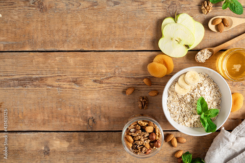 Ingredients for cooking healthy breakfast. Oatmeal  dried and fresh fruits  honey and nuts on a wooden table with copy space top view. Breakfast table concept