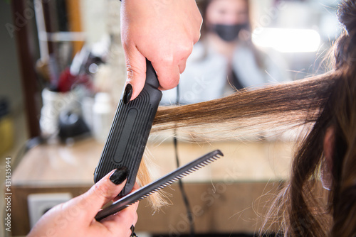 close-up of hands straightening hair with iron