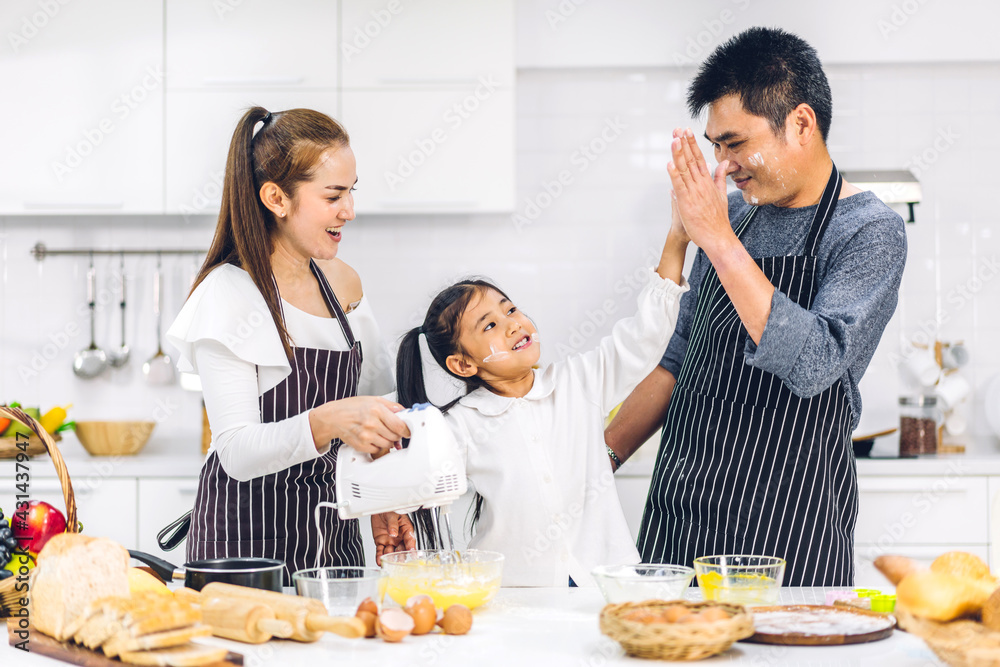 Portrait of enjoy happy love asian family father and mother with little asian girl daughter child having fun cooking food together with baking cookie and cake ingredient on table in kitchen