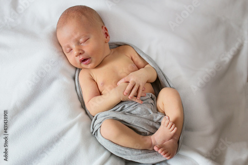 Newborn baby beautifully posing and sleeping. Sleeping newborn boy on a white background in a gray wrap.