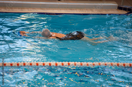 A woman swims in a black swimsuit and a swimming cap swims in the pool.