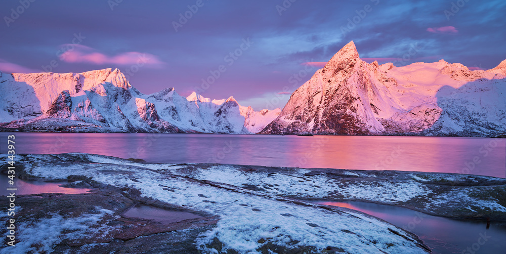 panoramic landscape on the Lofoten, Norway, with snow covered mountains and a fjord at sunrise