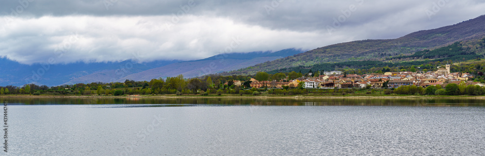 panorama of a high mountain village on the shore of the lake with large clouds in dramatic sky.