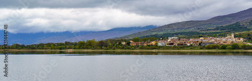 panorama of a high mountain village on the shore of the lake with large clouds in dramatic sky.