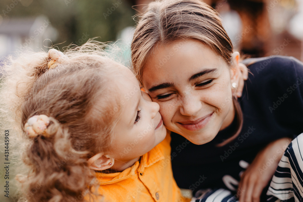 portrait of two cute little girls where a smaller curly girl hugs an older girl with freckles on her face portrait of two cute little girls where a smaller curly girl hugs an older girl with freckles on her face