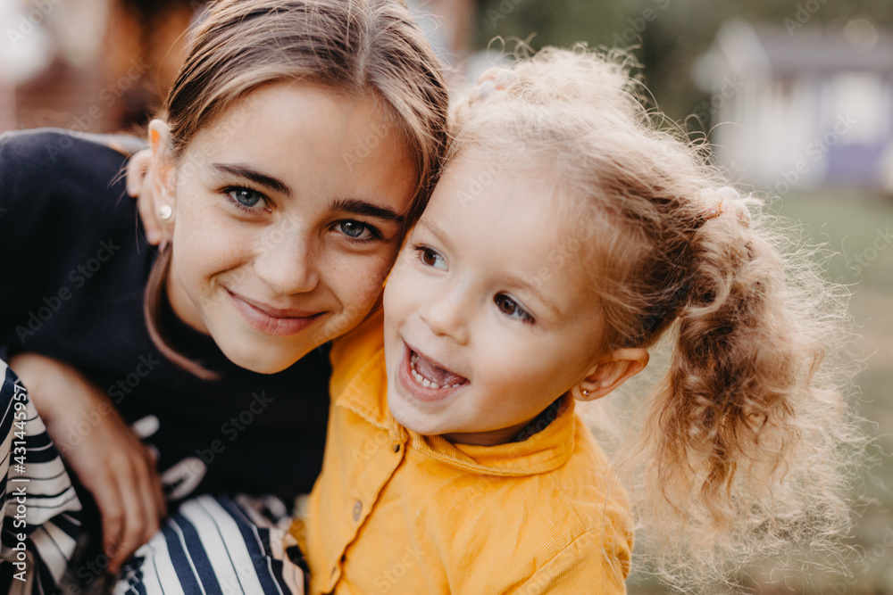 Obraz premium portrait of two cute little girls where a smaller curly girl hugs an older girl with freckles on her face