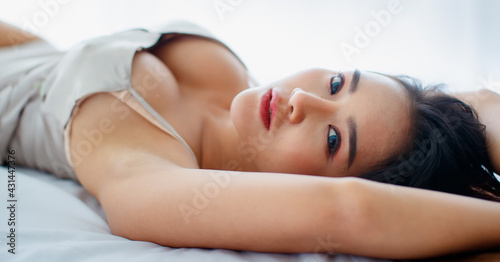 Beautiful young naughty girl with sexy pajamas seductively lie down on bed with ease to relax in bright tranquil morning of rest day and impassioned looking up to someone