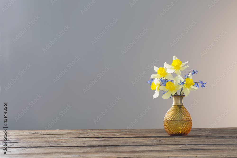 yellow narcissus and blue snowdrops in vase on wooden table on gray background yellow narcissus and blue snowdrops in vase on wooden table on gray background