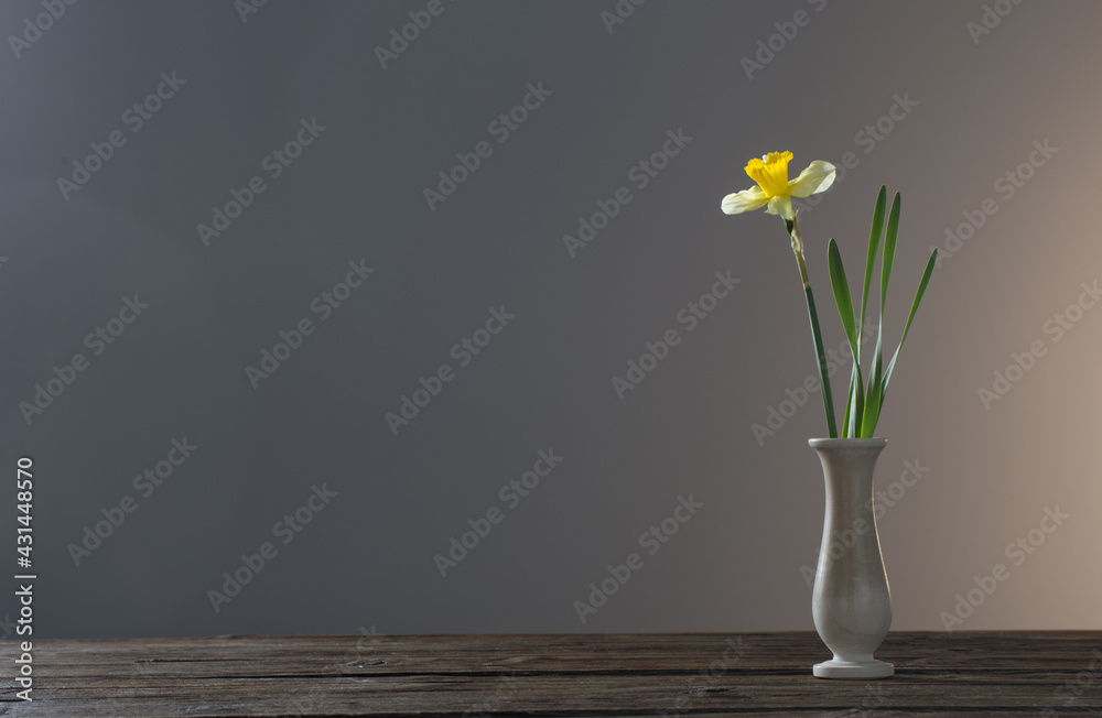 yellow narcissus in vase on wooden table on dark background yellow narcissus in vase on wooden table on dark background