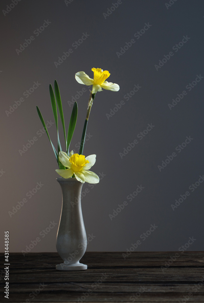 yellow narcissus in vase on wooden table on dark background yellow narcissus in vase on wooden table on dark background