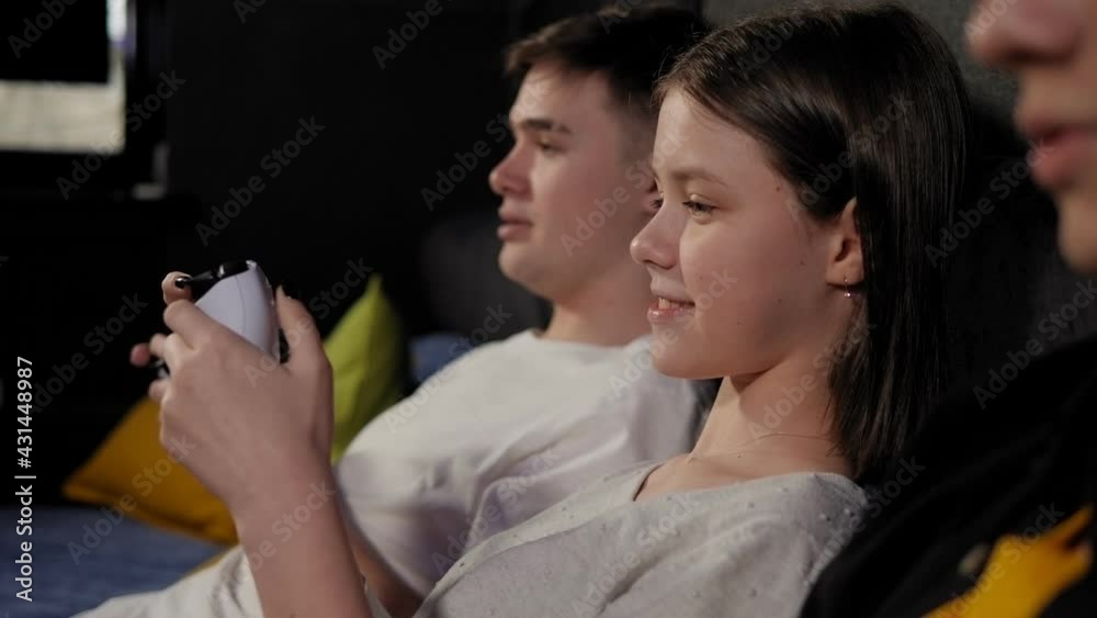 Three teenagers with joysticks play video games on the console sitting on a sofa Three teenagers with joysticks play video games on the console sitting on a sofa
