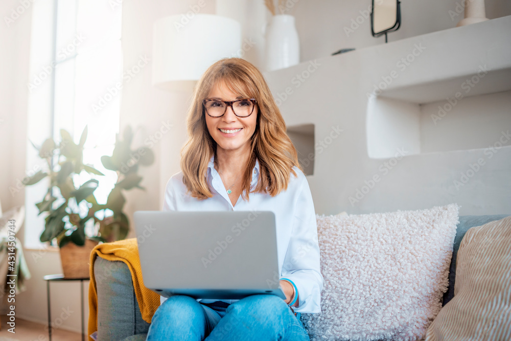 Happy middle aged woman using her laptop while sitting on the sofa at home Happy middle aged woman using her laptop while sitting on the sofa at home