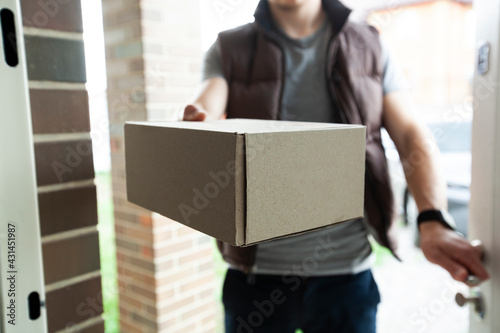 Deliveryman gives the carton box to the customer at the door of his house © SkyLine