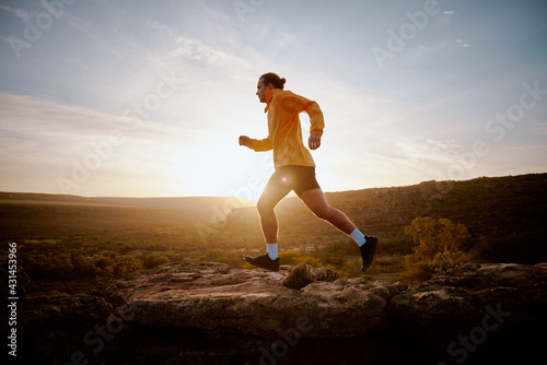 Fit young athlete man running up a hill during sunrise