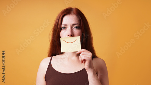 young woman hiding emotion with fake smile drawn on paper photo