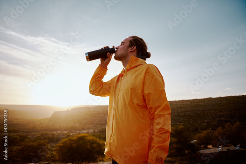 Low angle view of male athlete drinking water from bottle while resting after run