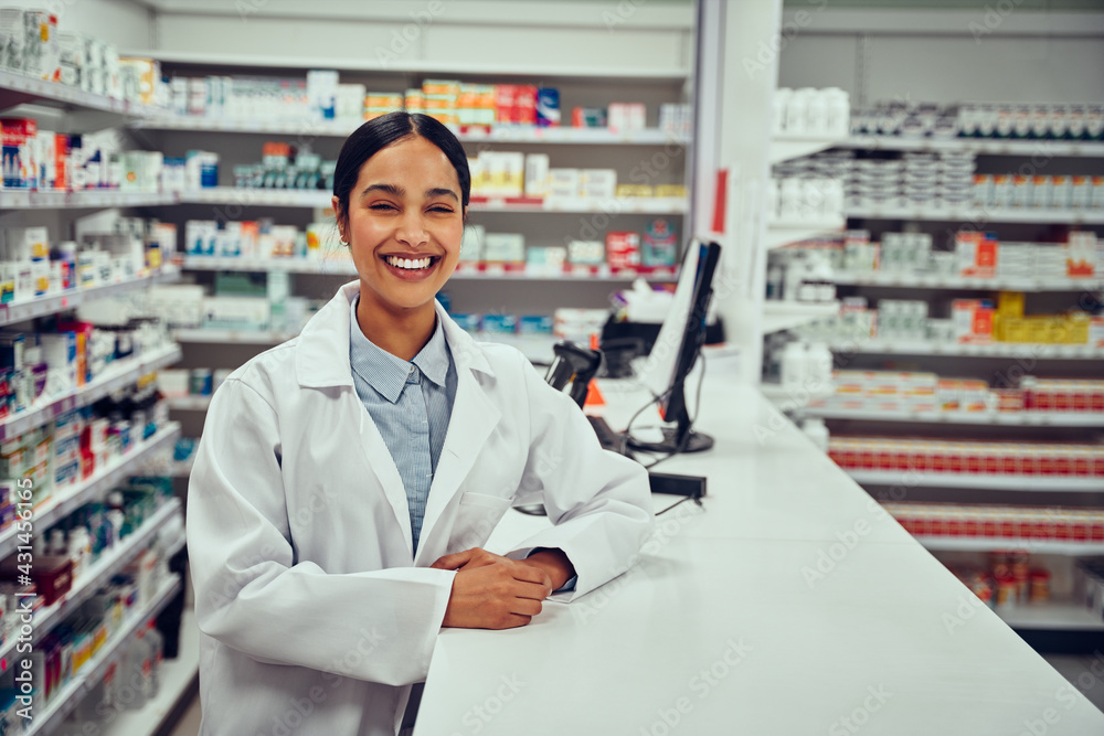 Portrait of smiling happy confident young woman pharmacist leaning on a desk in the pharmacy