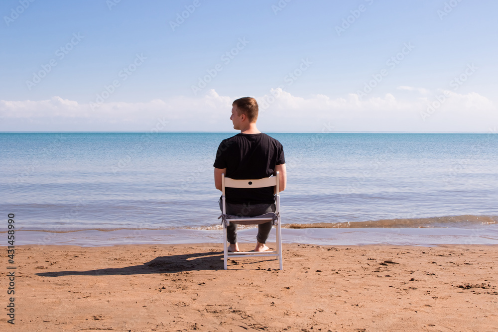 the guy sits on a white chair by the sea