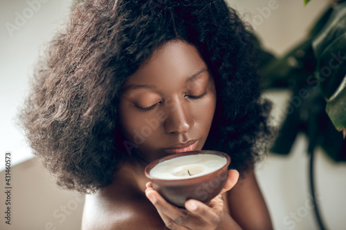 Naked dark-skinned woman smelling an organic candle