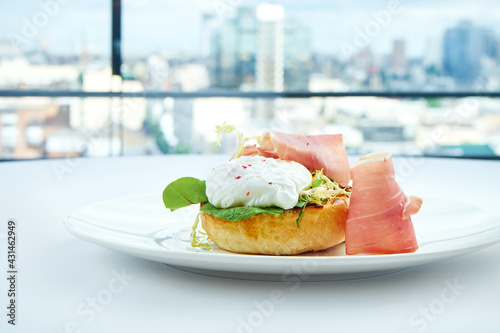 Delicious breakfast - toast with avocado, jamon crudo and poached egg, served in a white plate on a white tablecloth. Close up, selective focus