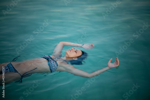Young adult woman in bikini lies relaxing in sea salt water with closed eyes
